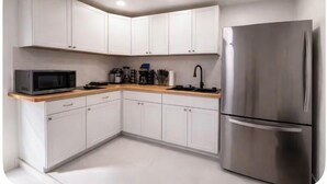 Een moderne keuken met witte kastjes, een roestvrijstalen koelkast, een magnetron en een houten aanrecht.