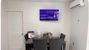 Een eethoek met een tafel, stoelen, een aan de muur bevestigde televisie en een airconditioning.
