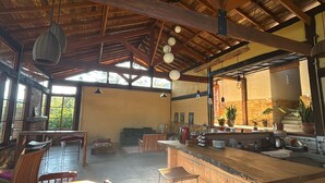 A spacious kitchen with a wooden ceiling, a dining area with a table and chairs, and a large window providing natural light. - Pousada Morada Canto do Sol (São Bento do Sapucaí)