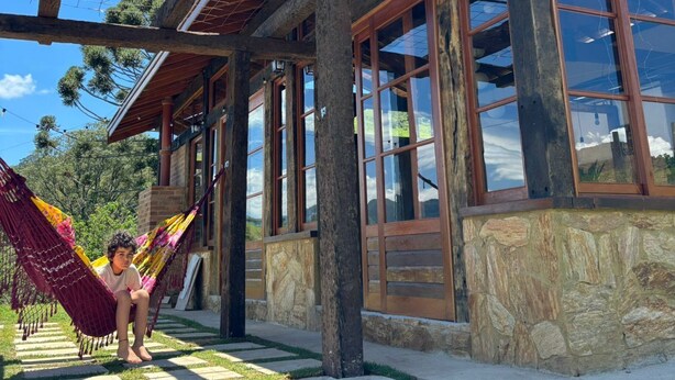 A modern house with a wooden porch, large windows, and a stone foundation. - Pousada Morada Canto do Sol (São Bento do Sapucaí)