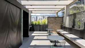 Um pátio moderno ao ar livre com mesa e cadeiras, uma parede de pedra e vista para edifícios ao fundo.