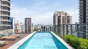 Piscina no terraço com espreguiçadeiras, cercada por edifícios altos.