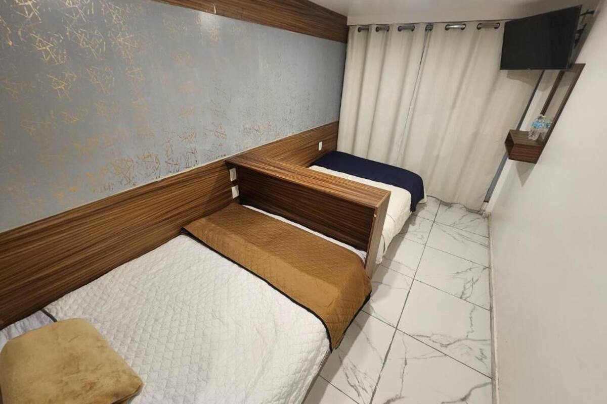 A bedroom with two beds, a wooden headboard, a flat-screen TV, and a curtain.