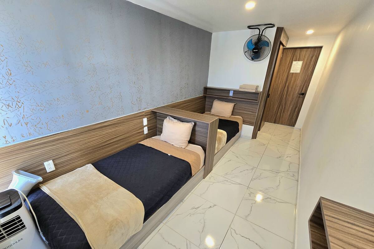 A hotel room with a bed, a fan, a heater, and a tiled floor.