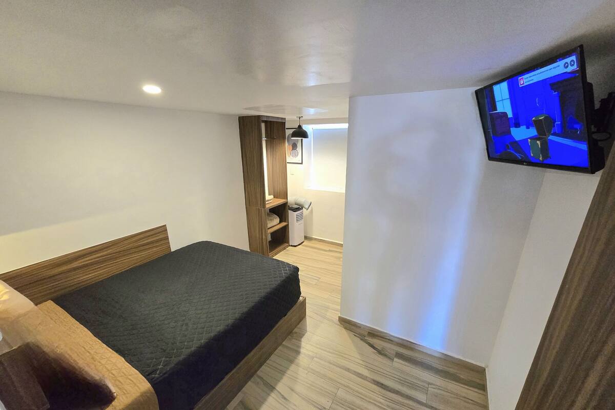 A room with a bed, a TV mounted on the wall, and a wooden wardrobe.