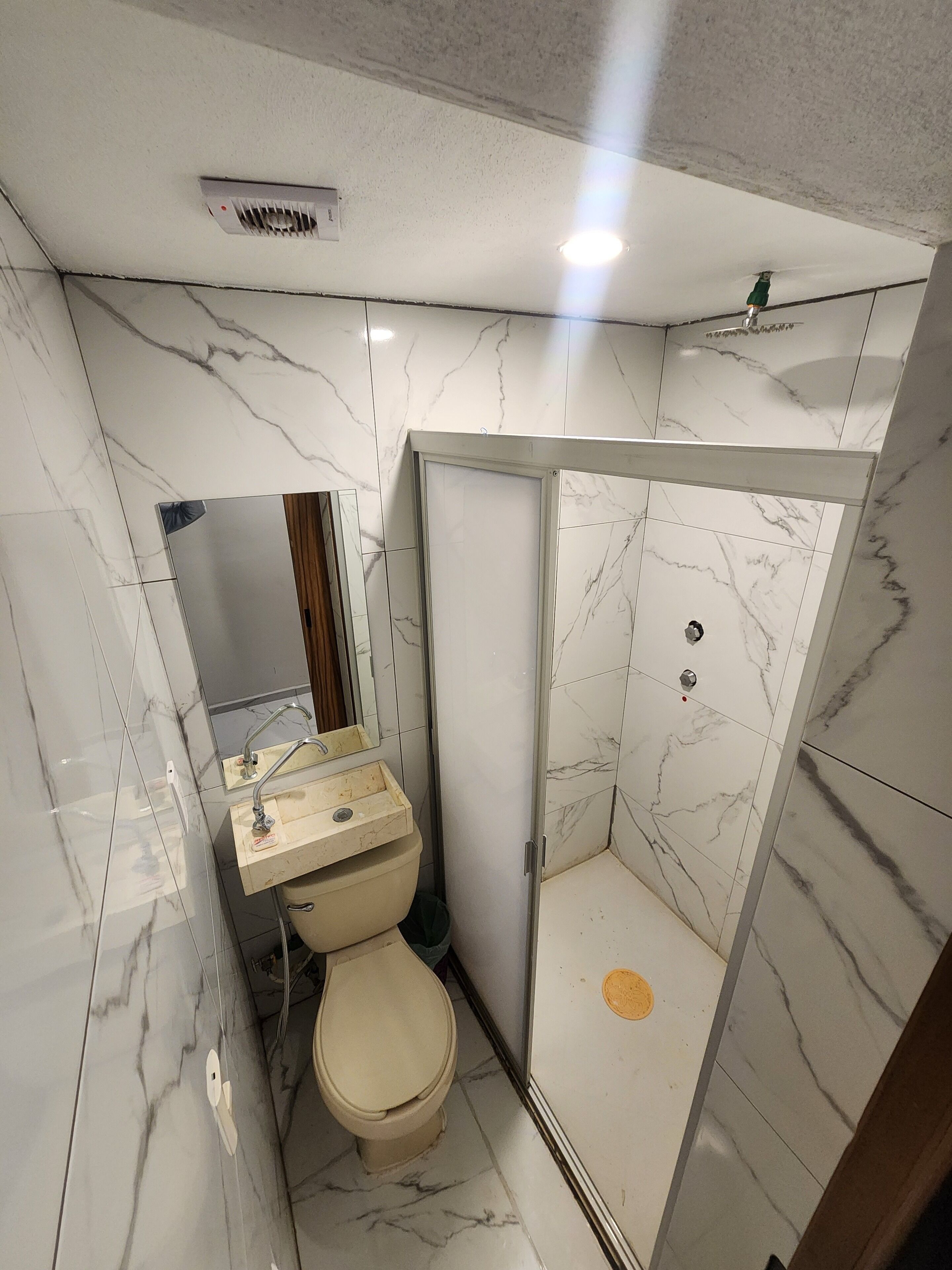 Een badkamer met toilet, wastafel en douche, geheel betegeld met marmer.