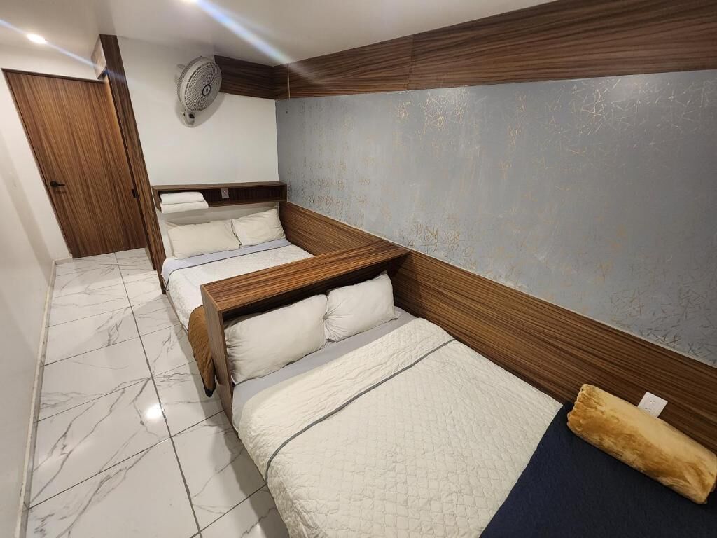 A hotel room with a wooden headboard, a marble floor, and a wall-mounted fan.