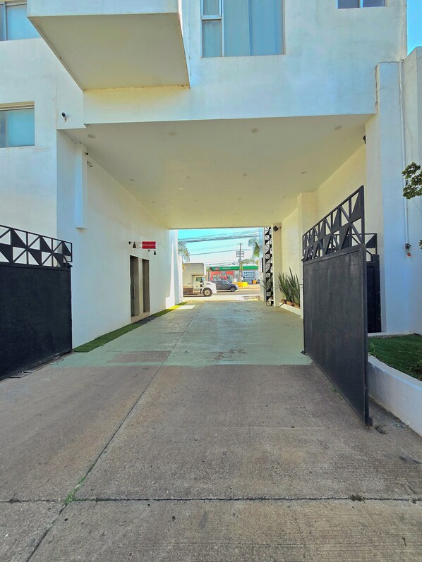 A building entrance with a gated driveway, a visible sign, and a parked vehicle in the background. - Alambique Hotel Express (Arandas)