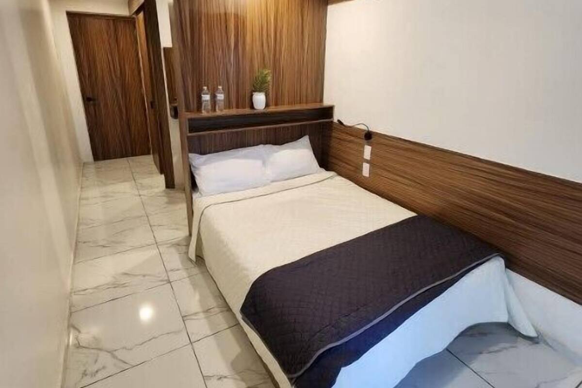 A hotel room with a bed, a wooden headboard, a marble floor, and a small plant on a shelf.