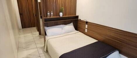 A hotel room with a bed, a wooden headboard, a marble floor, and a small plant on a shelf.