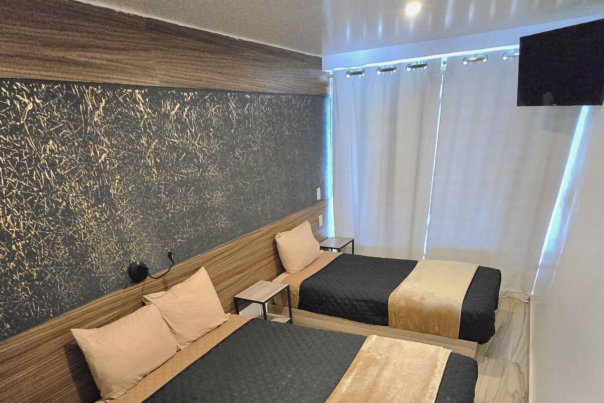 A hotel room with two beds, a wooden headboard, a small table, and a TV mounted on the wall.