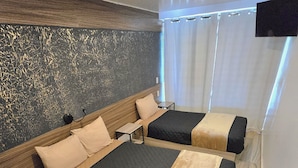 A hotel room with two beds, a wooden headboard, a small table, and a TV mounted on the wall.