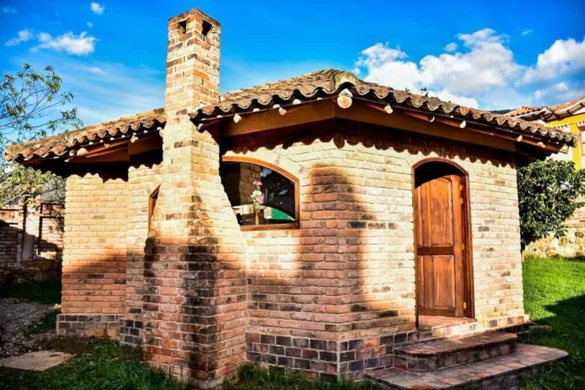 Una pequeña casa de ladrillo con chimenea, puerta de madera y ventana.