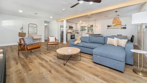 Ein großzügiges Wohnzimmer mit blauem Sofa, Ledersesseln, einem Holztisch und einem Deckenventilator.