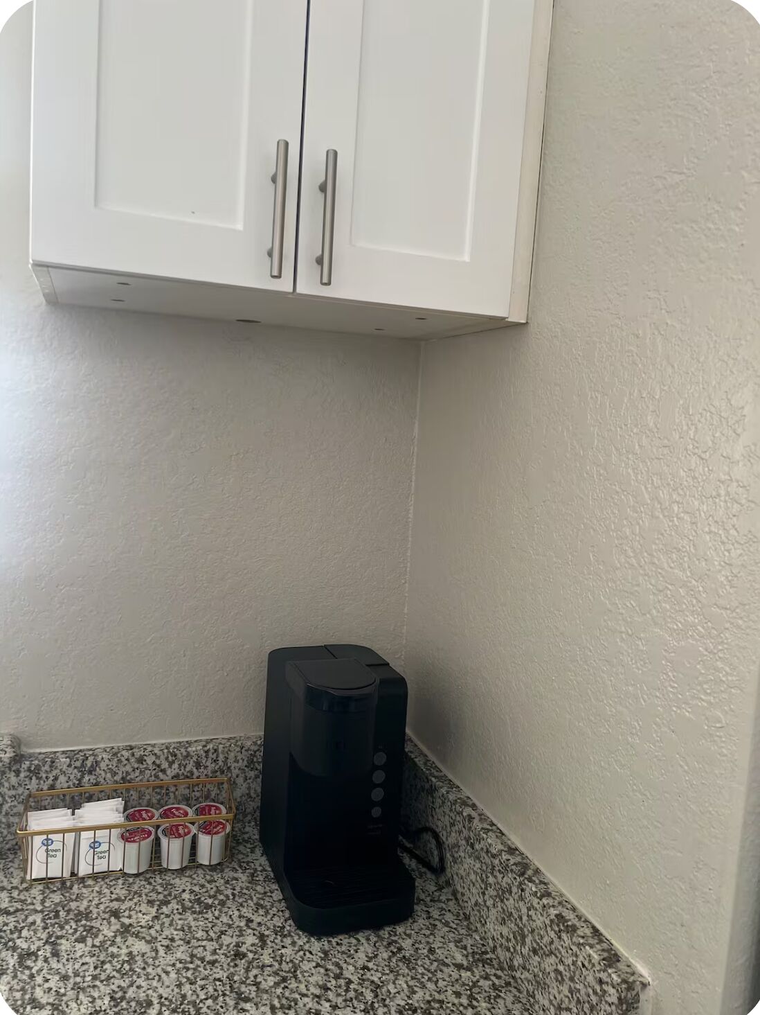 A kitchen with a coffee maker, a cabinet, and a container with tea bags.