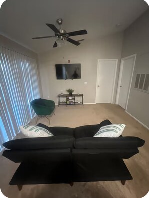 A living room with a black sofa, a ceiling fan, a TV, and a sliding door.