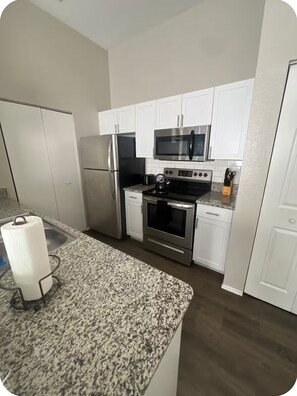 A modern kitchen with white cabinets, stainless steel appliances, and a granite countertop.
