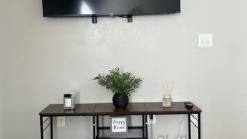 A flat-screen TV mounted on a wall, a dark wooden console table with a plant, a small candle, and a sign that says 'Happy Home.'