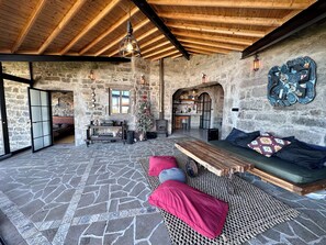 A rustic stone interior with a wooden ceiling, a stone fireplace, a wooden bench with cushions, and a wall-mounted decorative piece. - Casa de Arte Nordeste (Pedreira)