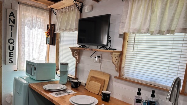 A kitchen with a microwave, coffee maker, and a TV on the wall.