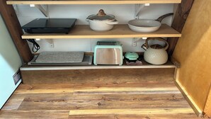 A kitchen with wooden shelves, a toaster, a kettle, and various dishes.