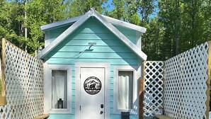 A small, light blue cabin with a white door, a 'NO SMOKING' sign, and a wooden deck leading to it.