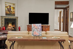 Un salon avec un canapé beige, une table basse en bois, une cheminée et un téléviseur à écran plat fixé au mur.