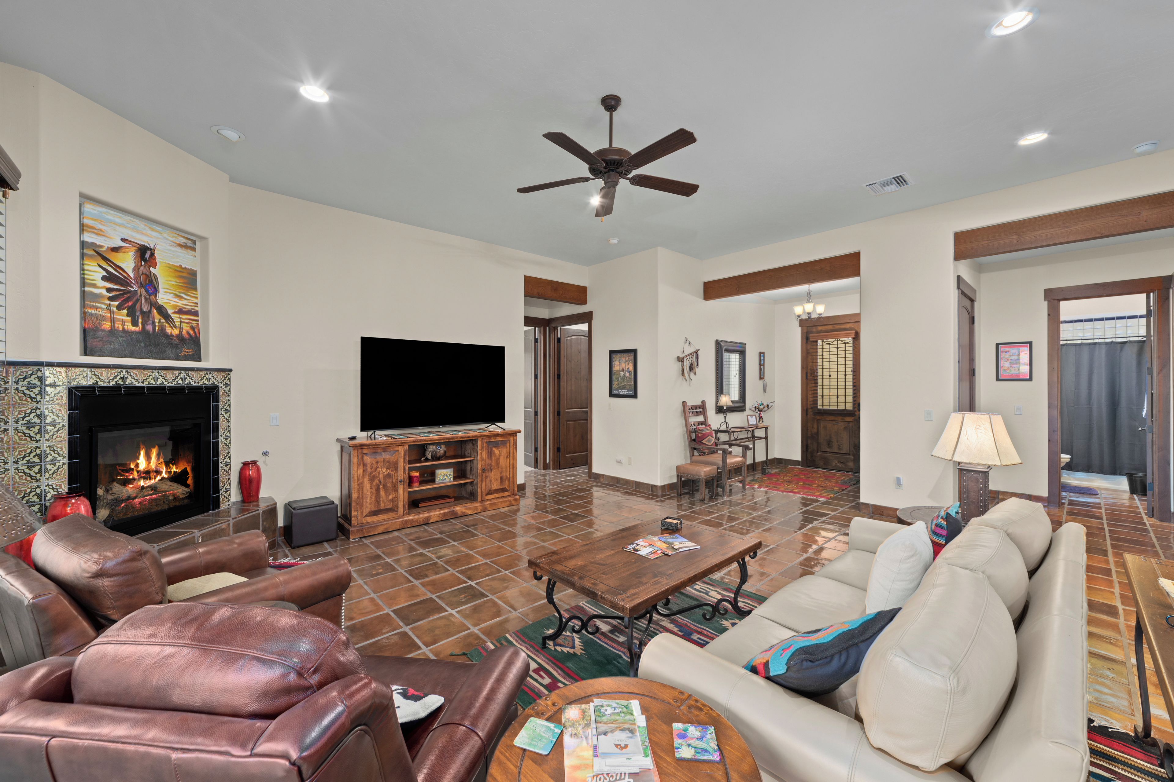 A spacious living room with leather sofas, a flat-screen TV, a fireplace, and a ceiling fan.