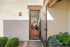 Une porte qui mène à un espace intérieur doté d’un sol carrelé, d’un tapis et d’une chaise.
