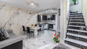 Un salon moderne avec un canapé, une table à manger et des chaises, une cuisine avec un pare-feu en marbre et un escalier agrémenté d’une plante en pot.