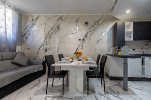 A modern living space with a dining table, black chairs, a sofa, and a kitchen area with a marble backsplash. - Room 'Camera Deluxe' with Wi-Fi and Air Conditioning (Nulvi)