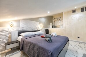 A modern bedroom with a bed, bedside tables, a nightstand, a mirror, and a towel rack.
