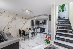 Ein modernes Wohnzimmer mit Sofa, Esstisch und Stühlen, eine Küche mit Marmor-Spritzschutz und eine Treppe mit einer Topfpflanze.