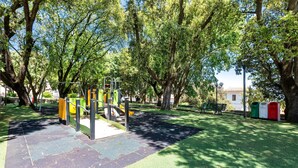 Un parc infantil amb aparells d'exercici, arbres i una bosc.