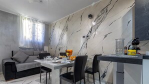 Zona menjador moderna amb paret amb dibuixos de marbre, un sofà, una taula de dinar amb cadires i una barra de cuina.