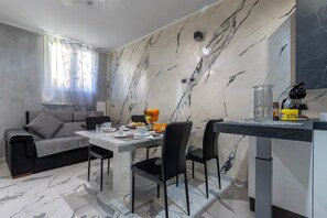 Ein moderner Essbereich mit Wand im Marmor-Design, einer Couch, einem Esstisch mit Stühlen und einer Küchenzeile.