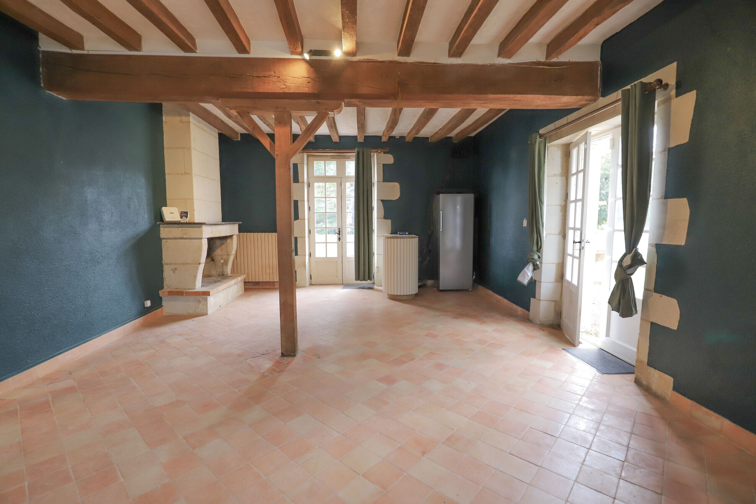 Ein geräumiger Raum mit Fliesenboden, Holzbalken an der Decke, einem Kühlschrank und einer Tür mit Fenster.