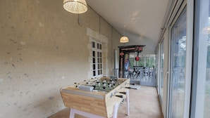 A foosball table in a room with a large window, a door, and a wall with a textured surface. - So Villa La Messagerie (49) - Heated pool - Basketball - 2 hours from Nantes - Sleeps 36. (Noyant)