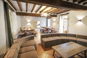 A spacious room with a high ceiling, exposed wooden beams, and a long dining table with benches. - Villa La Messagerie (49) — Heated pool — Basketball — 2 hours from Nantes — Sleeps 36. (Noyant)