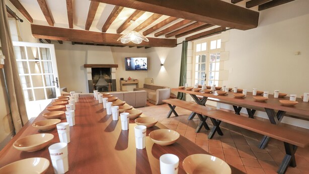 A long dining table with multiple bowls and cups, a television, and a fireplace in the background. - So Villa La Messagerie (49) - Heated pool - Basketball - 2 hours from Nantes - Sleeps 36. (Noyant)