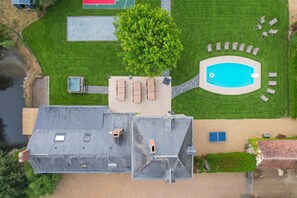 Vue aérienne d’une propriété dotée d’une piscine, de chaises longues et d’un grand arbre.
