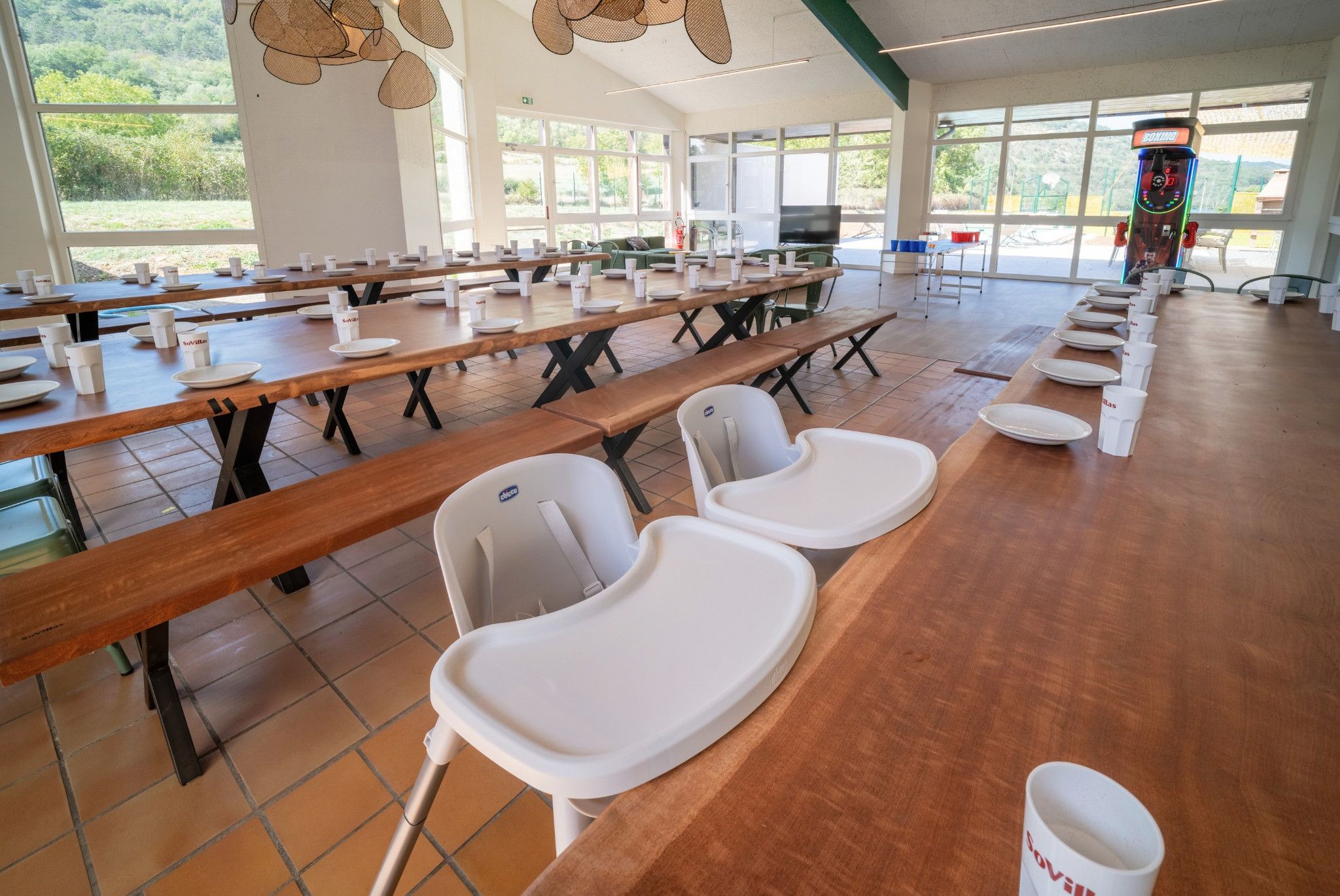Una cafeteria amb taules de fusta llargues, caires blanques i una màquina expenedora.