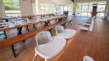 Una cafeteria amb taules de fusta llargues, caires blanques i una màquina expenedora.