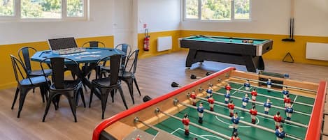 Una habitación con mesa de fútbol, mesa de billar y comedor con sillas y una mesa.