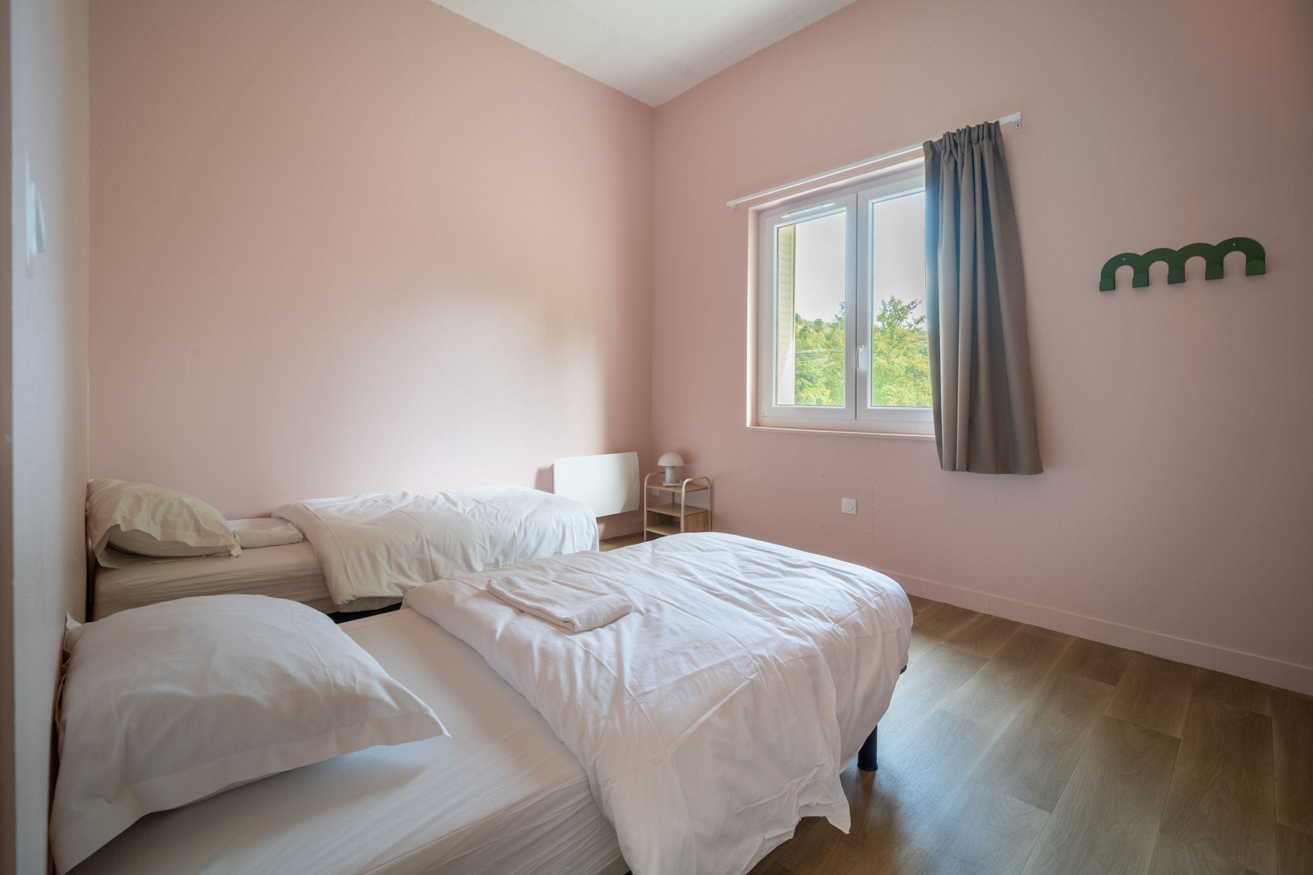 Een slaapkamer met twee bedden, een raam met gordijnen en een wandplank met een lamp.