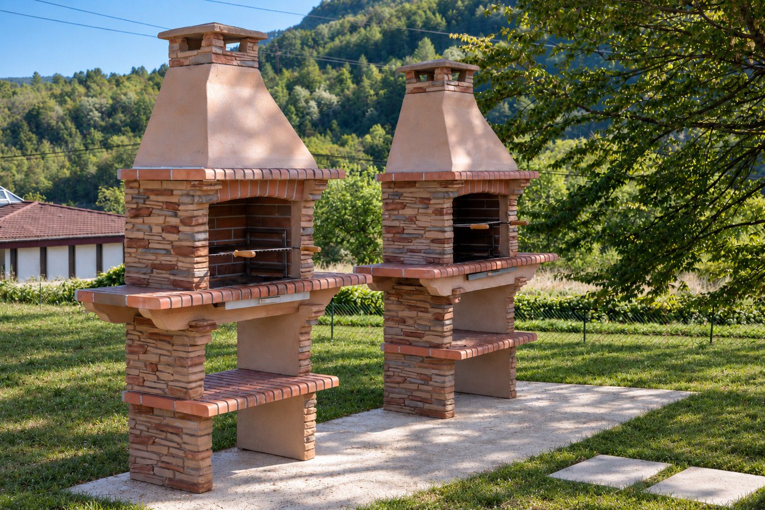 Deux fours à pizza en briques, installés à l’extérieur sur une dalle de béton dans un espace verdoyant, avec une base en pierre, un grillage et des arbres en arrière-plan.