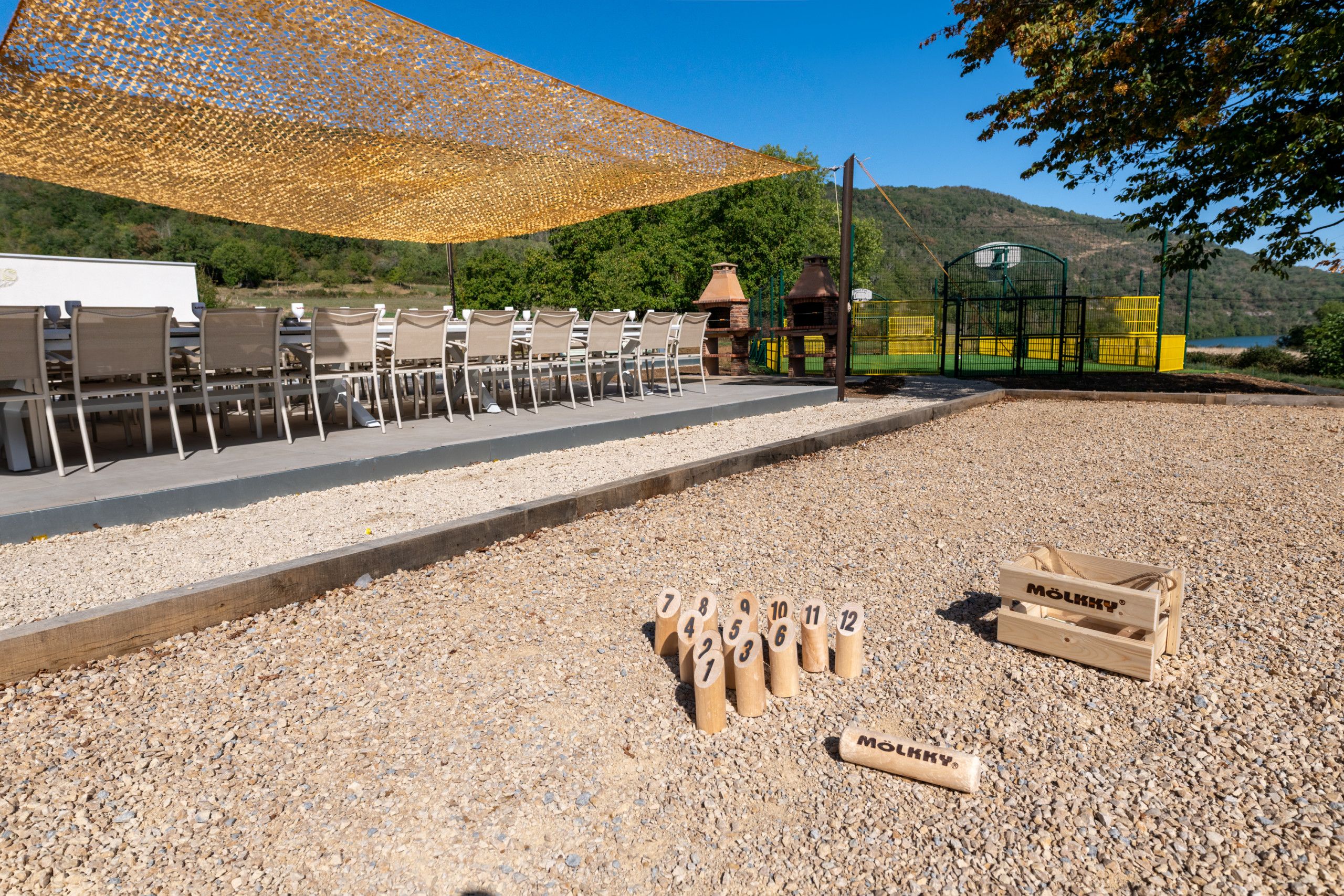 An outdoor dining area with tables and chairs, a barbecue grill, and a netted canopy.