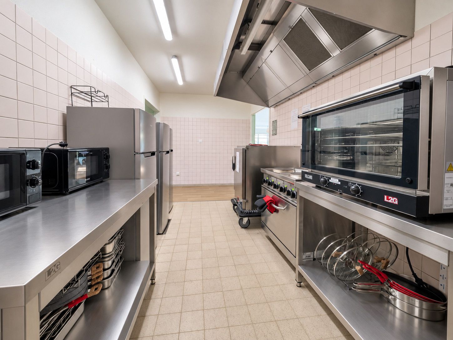 Une cuisine professionnelle équipée d’appareils en acier inoxydable, notamment un four à micro-ondes, des fours et une grande cuisinière industrielle.