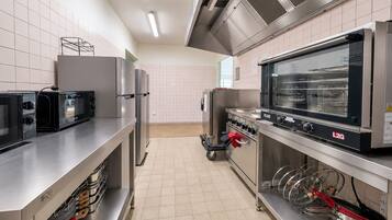 Une cuisine professionnelle équipée d’appareils en acier inoxydable, notamment un four à micro-ondes, des fours et une grande cuisinière industrielle.