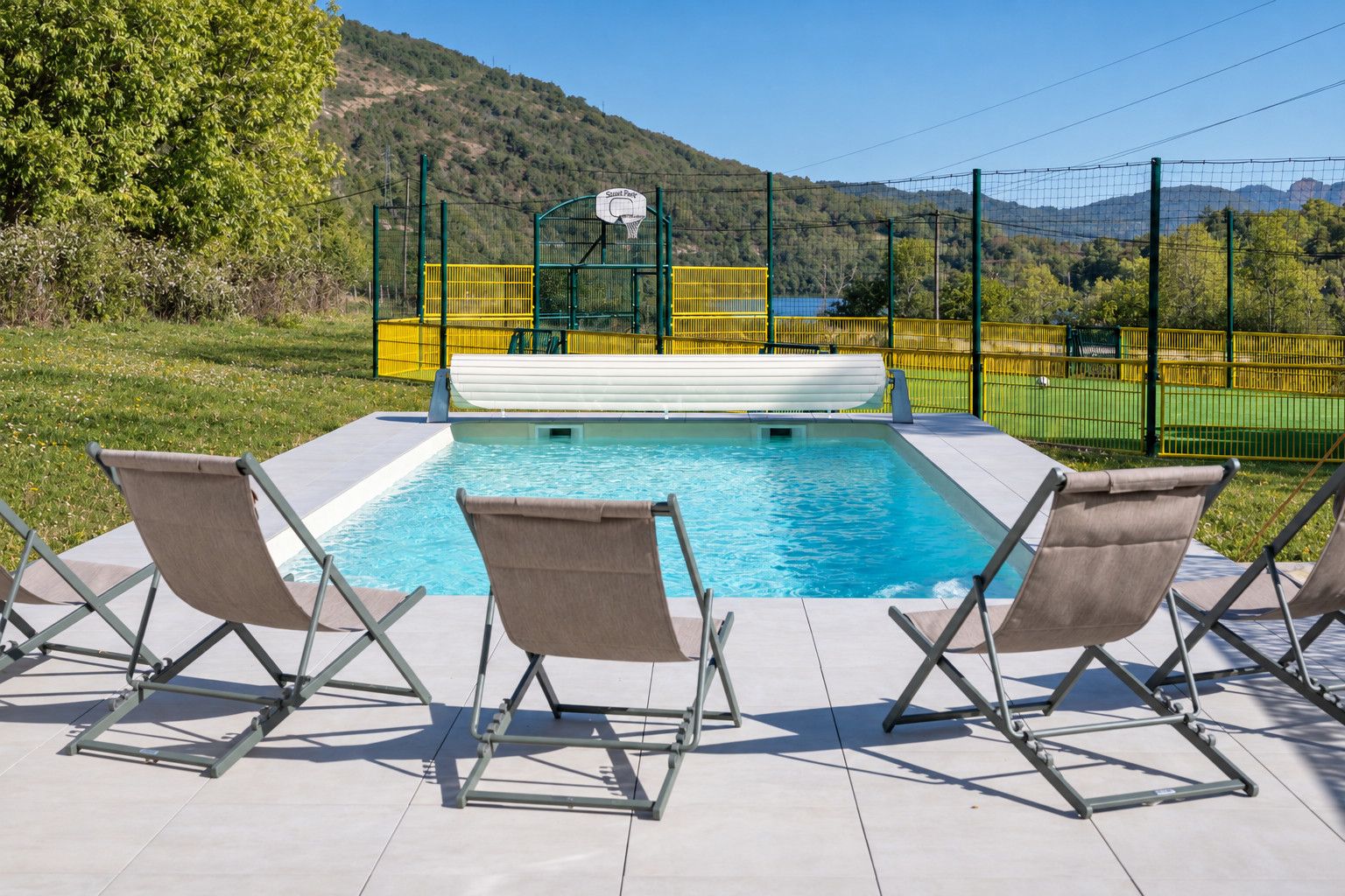 Ein Schwimmbecken mit Basketballkorb, umgeben von einem Zaun und Stühlen.